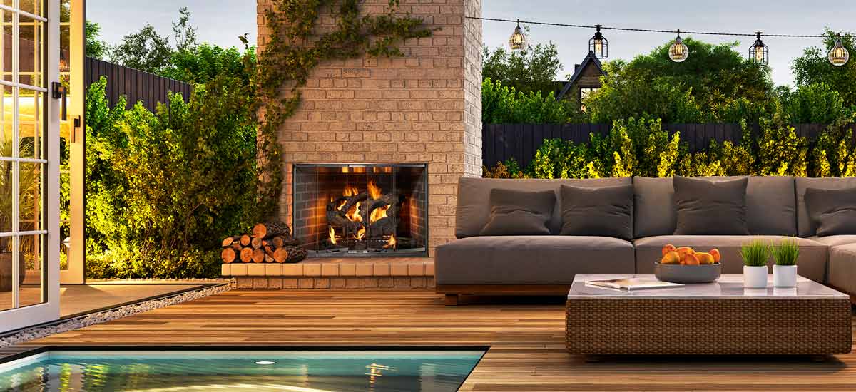 Gas logs burning in brick outdoor fireplace on patio with brown sofa to right and pool in front
