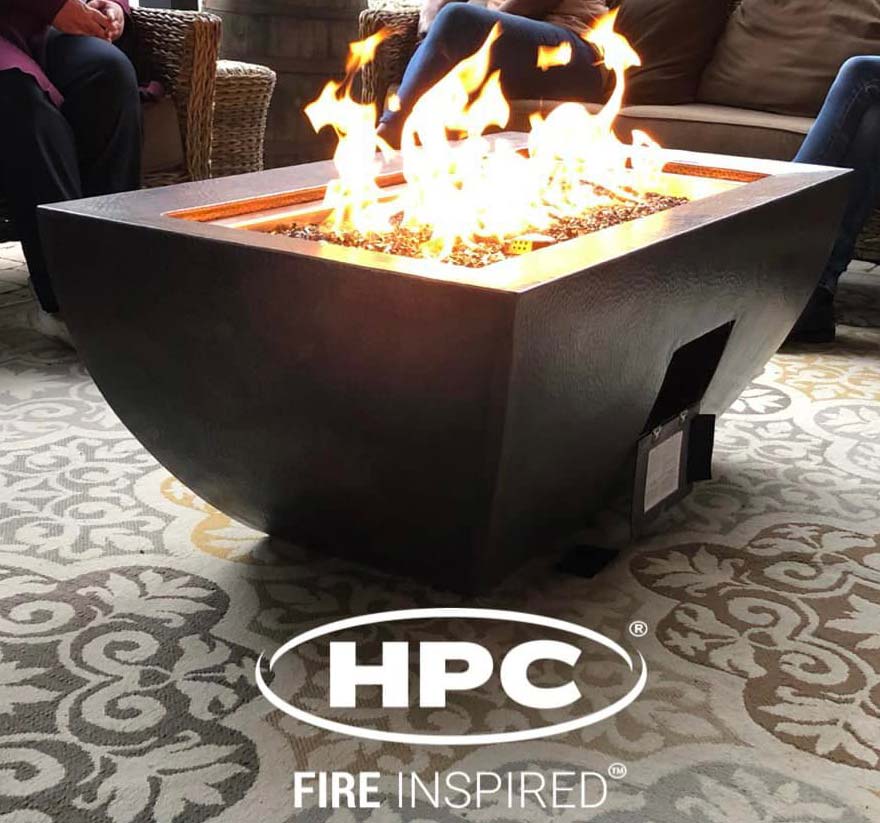 Oil rubbed, hammered copper rectangular fire bowl with open access door burning on patio with outdoor rug underneath.