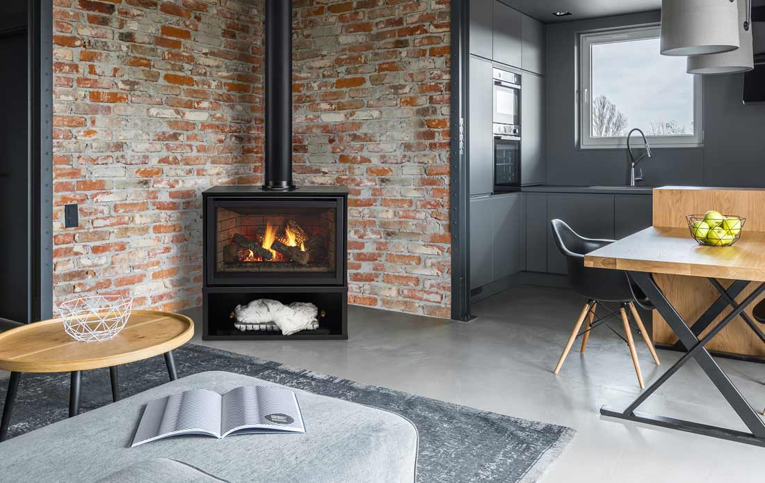 Majestic Trilliant freestanding gas fireplace in cabinet in front of brick wall in slate gray industrial loft