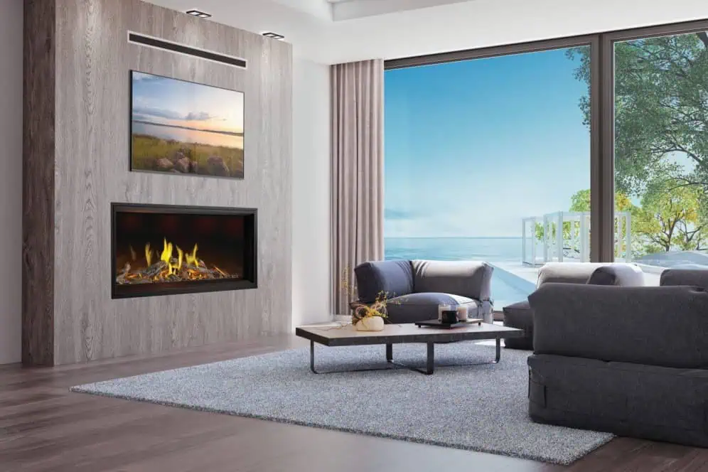 Napoleon Tall Vector gas fireplace with Luminous Logs burning on wood wall with TV above, floor to ceiling windows overlooking ocean, wood floor, grey furniture