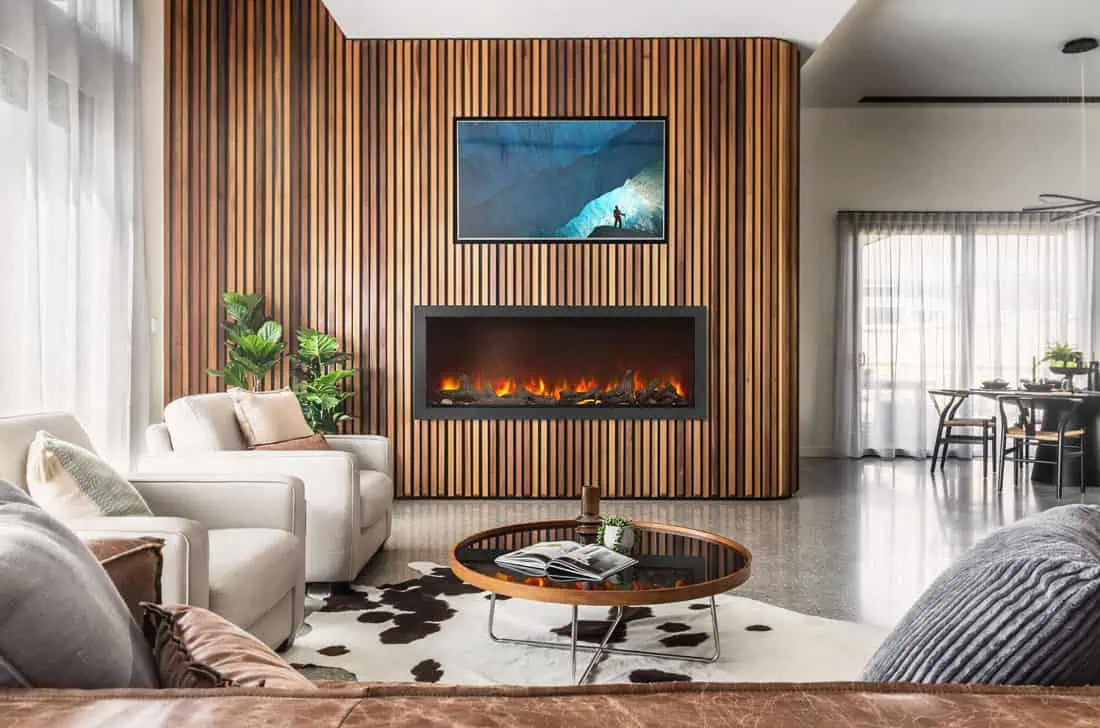 Napoleon Astound built-in linear electric fireplace on vertical wood slat wall, TV above in living room with white furniture cow hide rug.