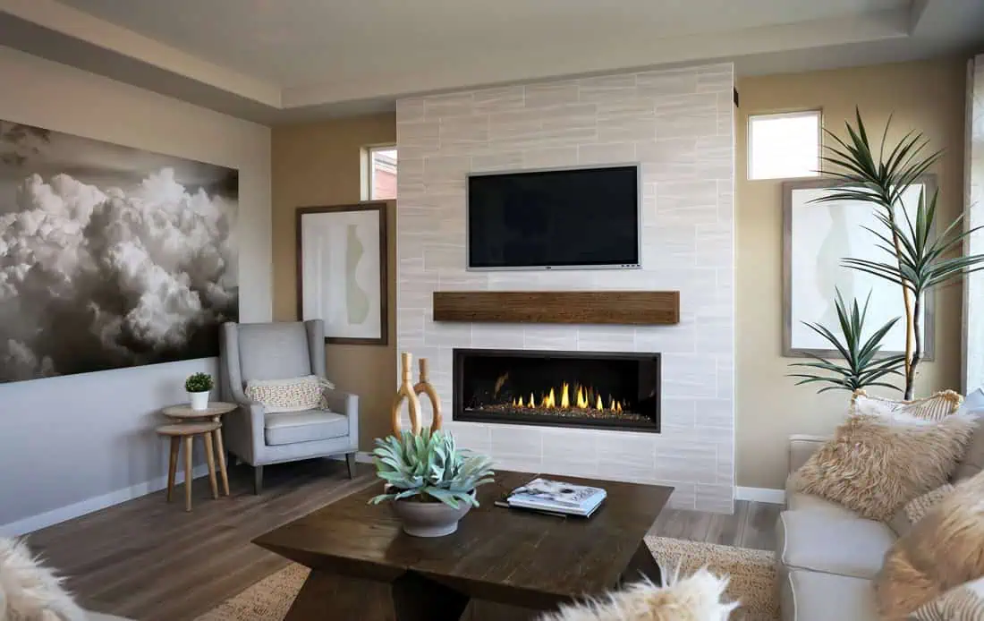 Napoleon Ascent Linear Premium 56 gas fireplace shown in light gray tile fireplace with wood beam mantel and TV above in beige living room with gray wingback chair to side.