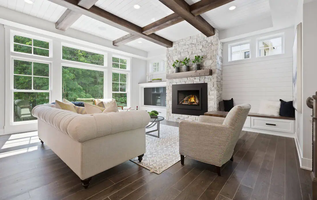 Napoleon Rosedale gas insert installed in living room white stone fireplace with white shiplap walls and brown ceiling beams and light furniture and rug on wood floor