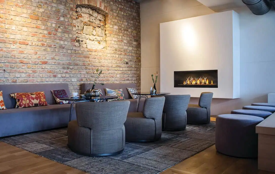 Napoleon Luxuria gas fireplace on white wall with banquet seating on adjacent brick wall, small tables and gray barrel chairs