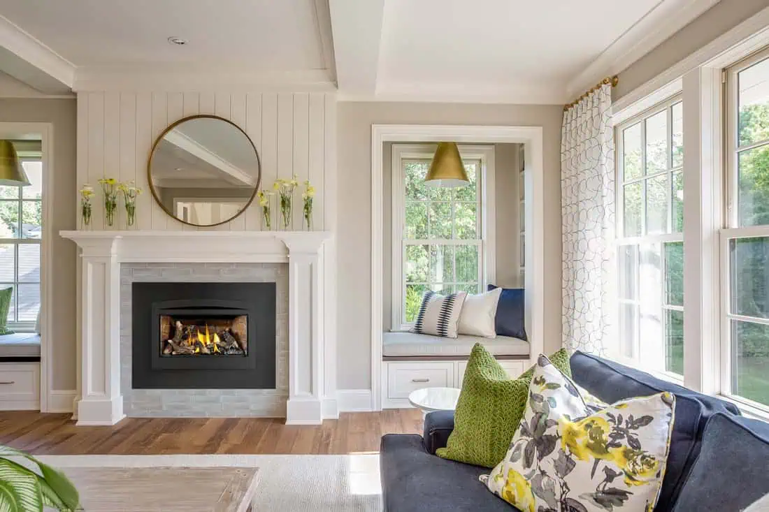 Napoleon Rosedale RD2NE gas fireplace insert in living room fireplace flanked by window seats, pale grey walls, white millwork, blue sofa, green accents, lots of windows